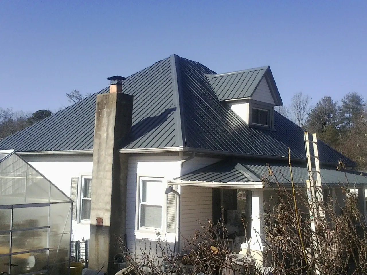 Dark blue standing seam metal roof on a white farmhouse with dormer — Slate & Tile Roof Repair by Roofing Brothers in Eaton Rapids