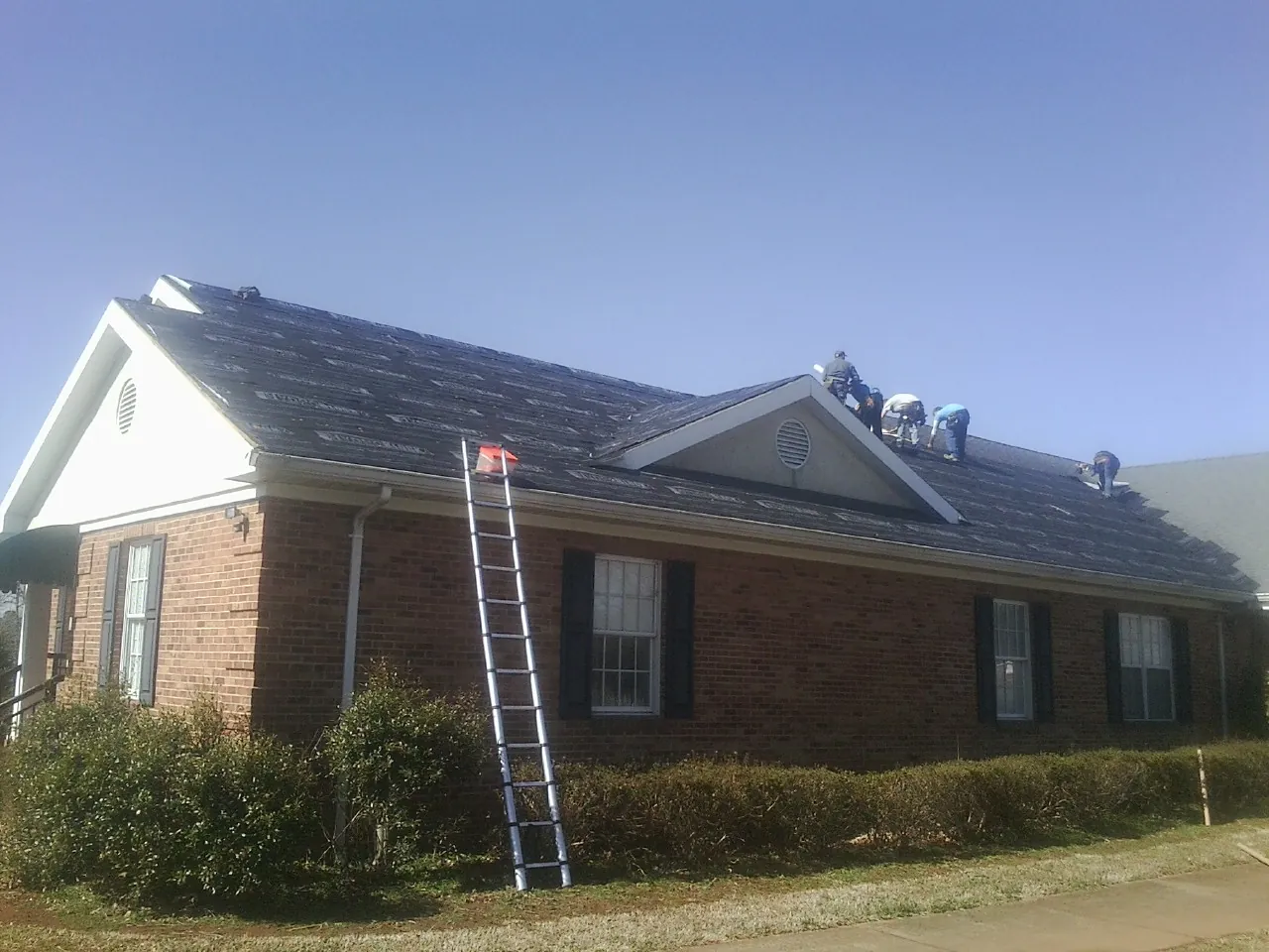 Crew tearing shingles off a brick ranch roof with a ladder set — Metal Roof Repair work by our crew in Eaton Rapids