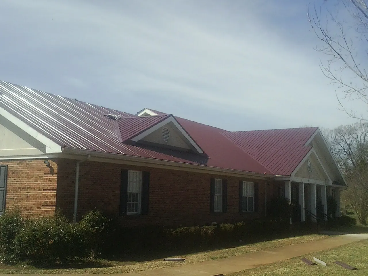 Red metal roof with gabled entries on a long brick building, from a Hail Damage Roof Repair job in Eaton Rapids