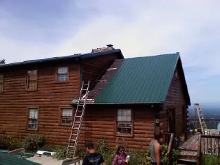 Green metal roof going on a two story log home with ladders set in Eaton Rapids