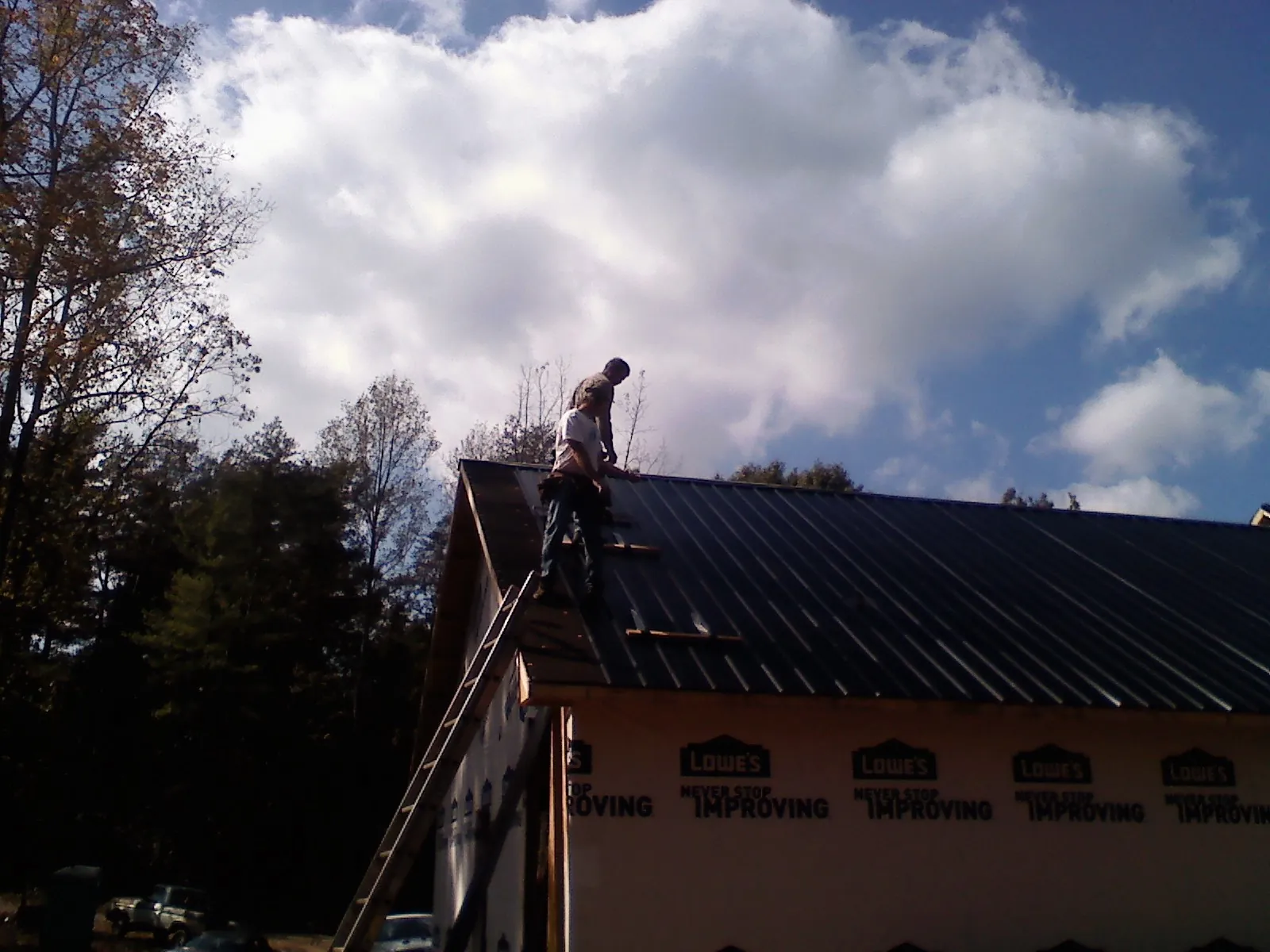 Roofer fastening dark metal panels high against a cloudy sky, from a Roof Inspection job in Eaton Rapids