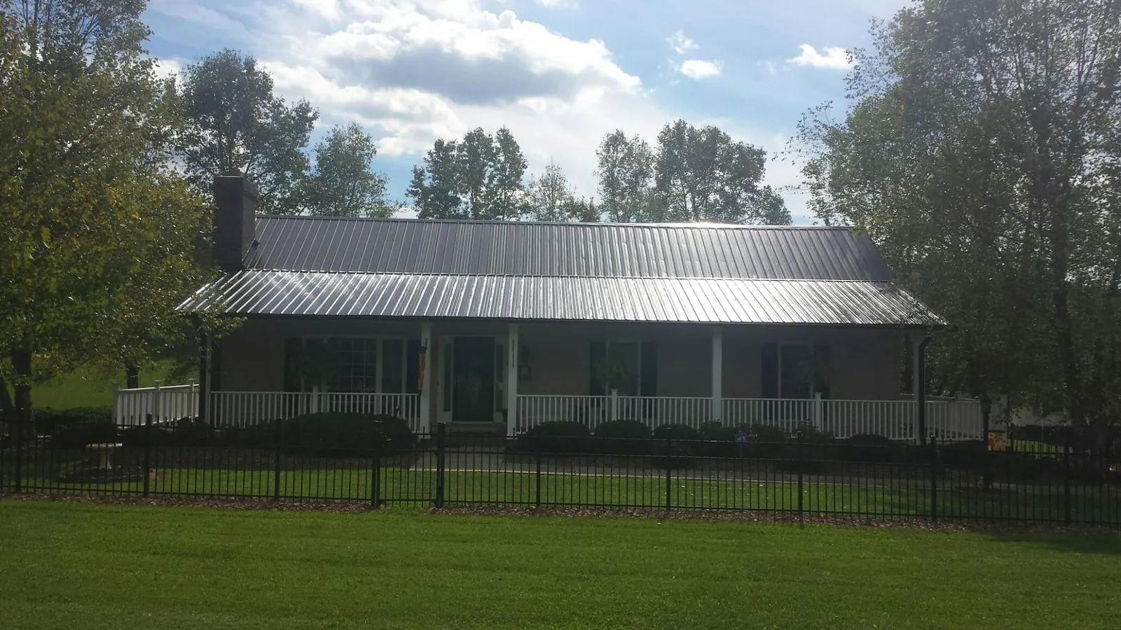 Gray metal roof on a brick ranch with a full width front porch — Gutter Guard Installation work by our crew in Eaton Rapids