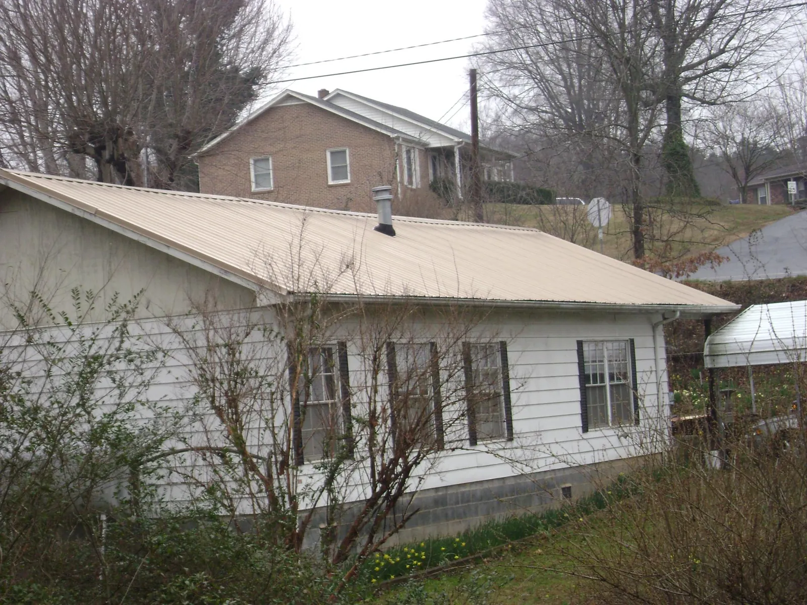 Tan metal roof on a white sided house set into a hillside — Commercial Roofing by Roofing Brothers in Eaton Rapids