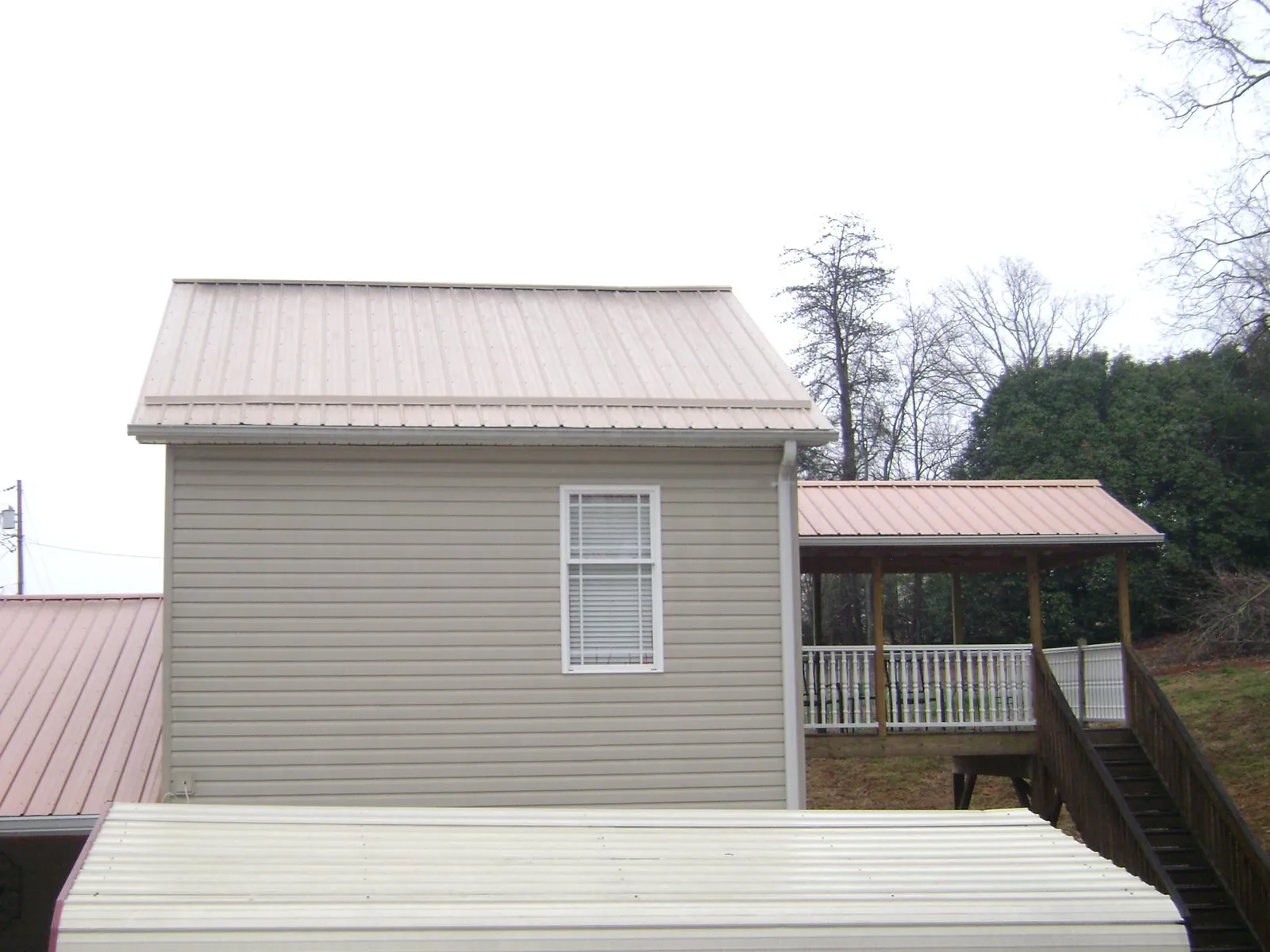 Tan metal roofs on a two story addition and attached porch, from a Roof Replacement job in Eaton Rapids