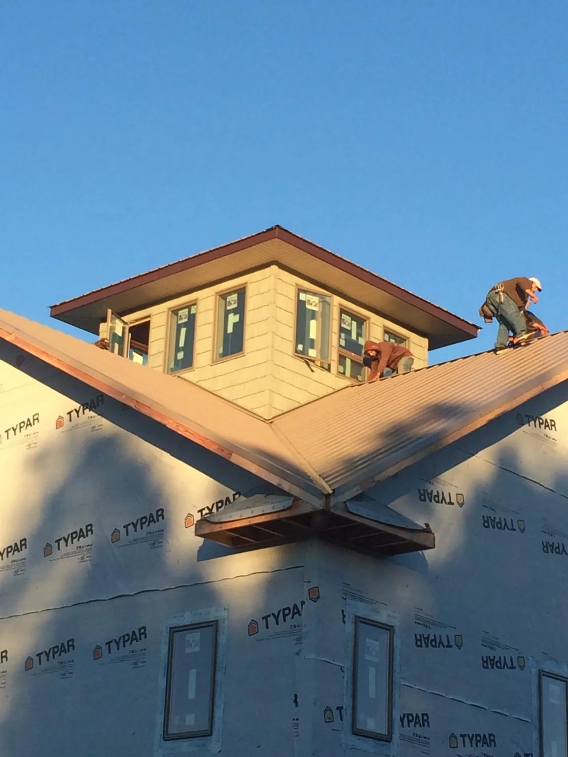 Roofers working around a rooftop cupola on a new metal roof at sunset — Roof Waterproofing in Eaton Rapids by Roofing Brothers